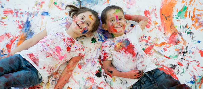 Two children laying on the floor covered in colourful paint